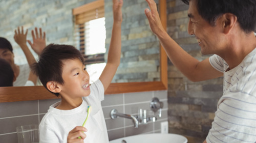 Father and son high-fiving in bathroom after morning toothbrushing routine in Glendale CA