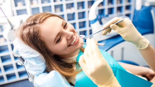 Smiling young woman receiving a dental cleaning exam in a dentist's chair